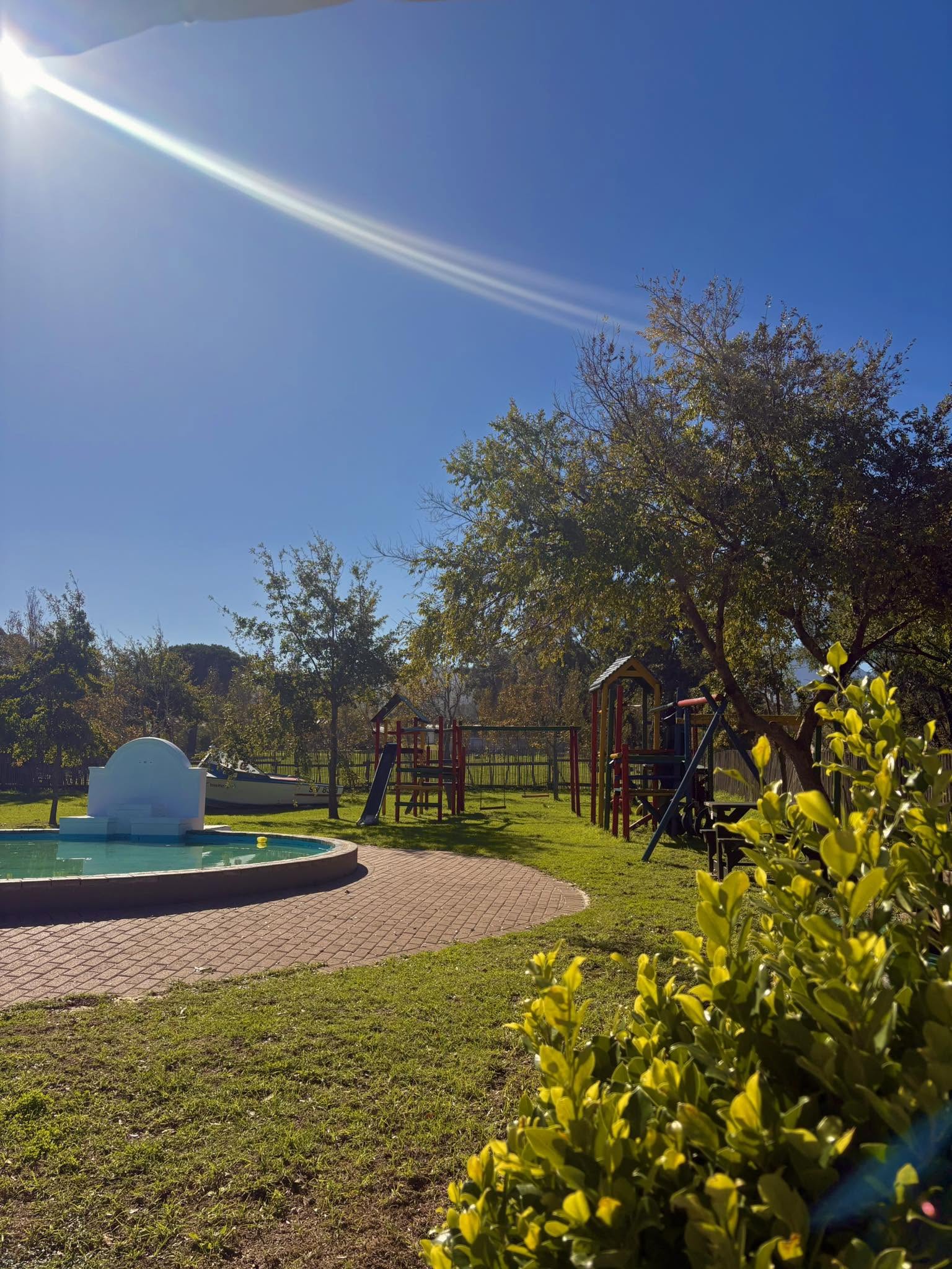 Outdoor play area with pool, trees and playground equipment